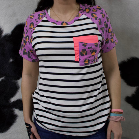 Short sleeve shirt with white and black vertical stripes, purple leopard print collar and sleeves and a double layered chest pocket with one being hot pink and the other being purple leopard print. 