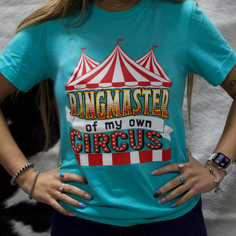 Model wearing teal t-shirt with circus graphic on the front.