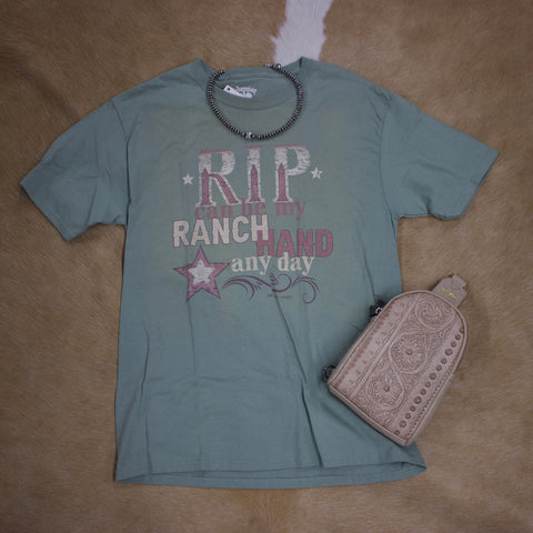Flat lay view of green t shirt with pink and cream lettering. Necklace and purse are laying next to shirt. 
