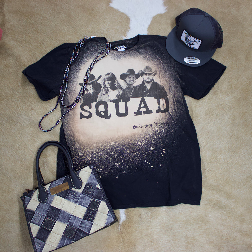 Flat lay view of bleached black t shirt with hat, necklace, and purse sitting next to it. 