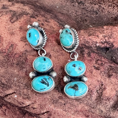 Turquoise and silver earrings on a textured brown surface
