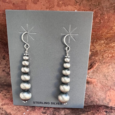Pair of sterling silver pearl earrings on a gray card with a textured brown background