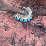 Silver Feather ring with turquoise stones on a textured stone surface