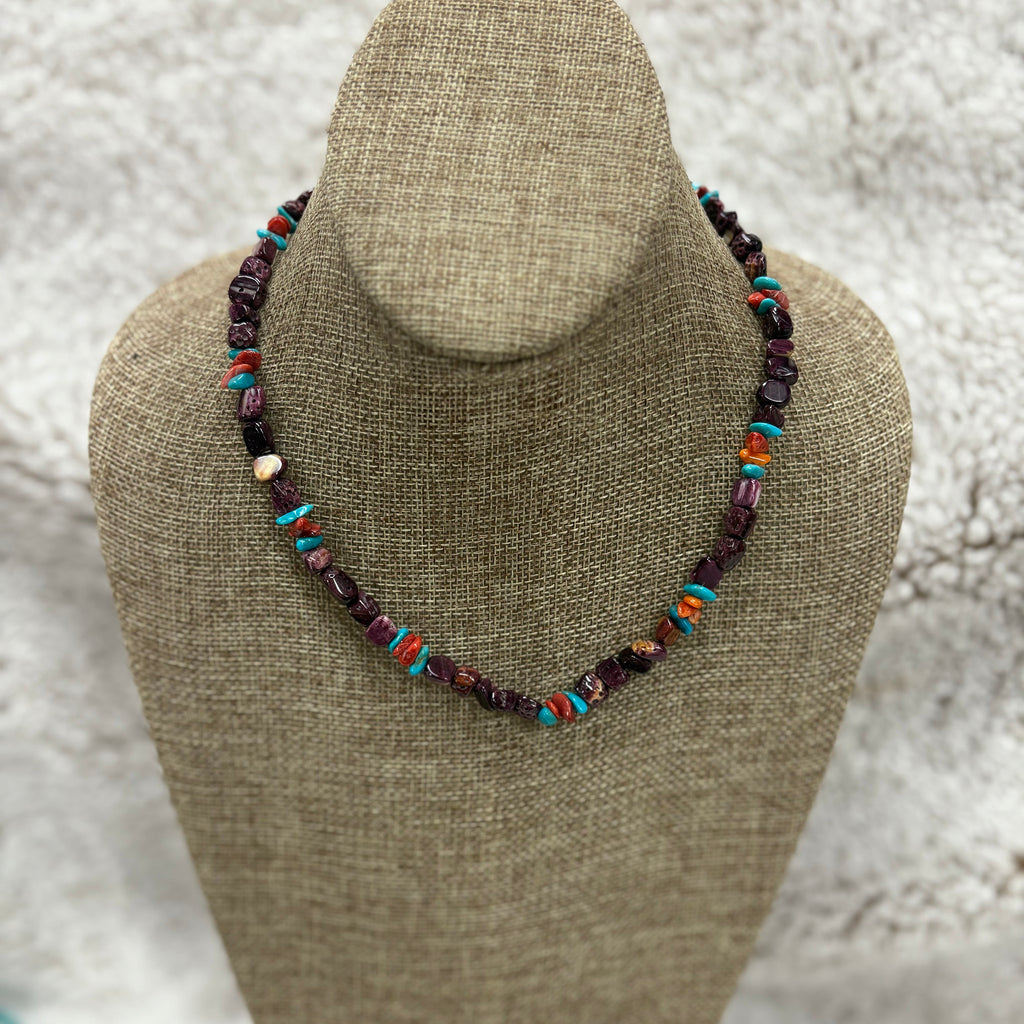 Purple beaded necklace with turquoise, red, and orange beads sitting on a mannequin 