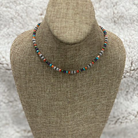Red, orange, green, turquoise, purple, and silver beaded necklace sitting on mannequin 