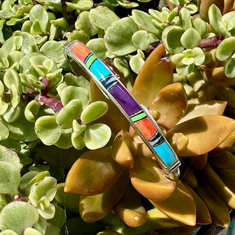 Multicolored bracelet with inlaid stones on a background of green and brown leaves