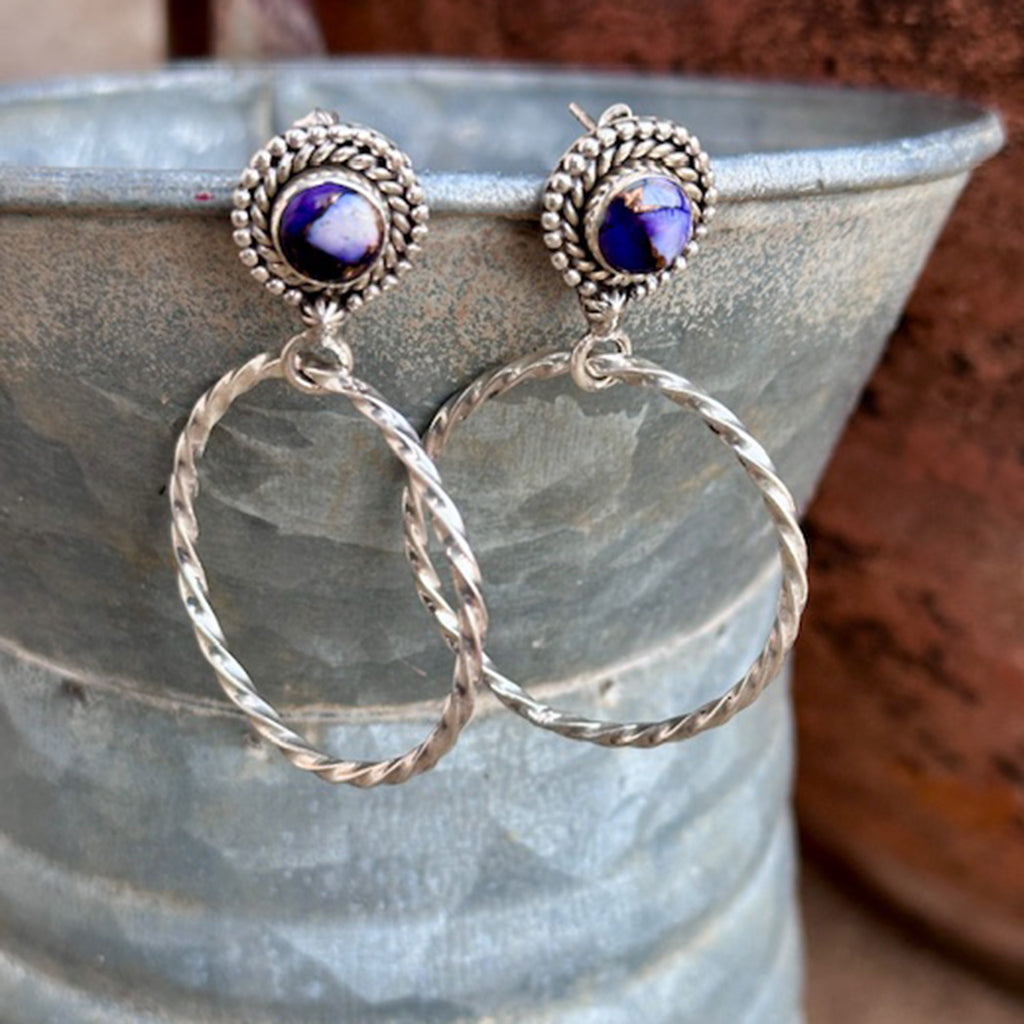 Silver hoop earrings with purple gemstones on a textured surface