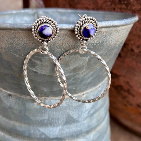 Silver hoop earrings with purple gemstones on a textured surface