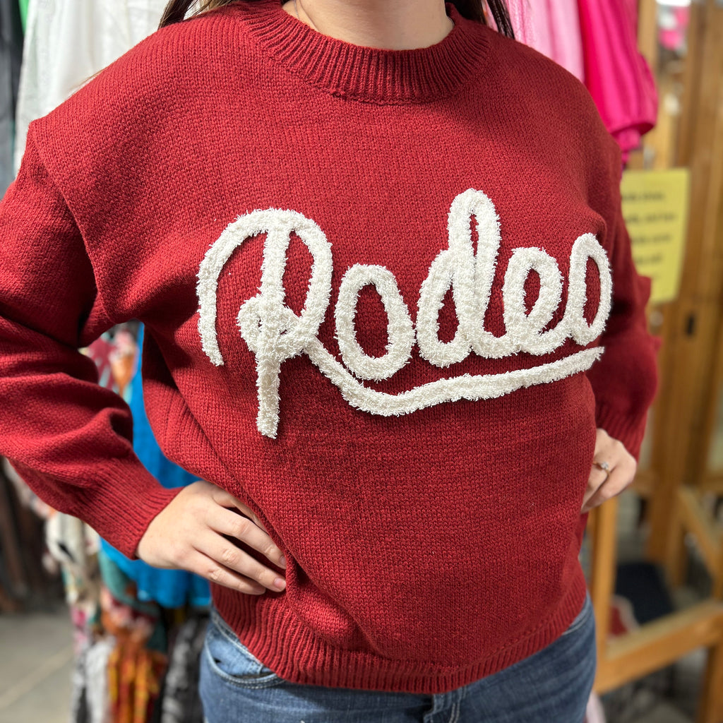 Red knit sweater with white cursive applique that says Rodeo