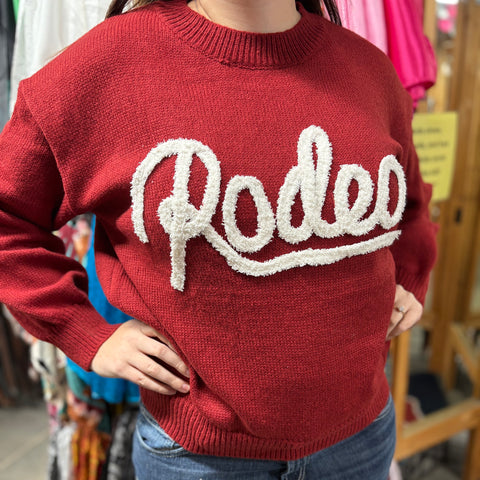 Red knit sweater with white cursive applique that says Rodeo