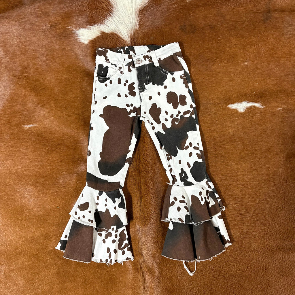 Flat lay picture of the front of the jeans, white jeans with black and brown cow spot patterns in a bell bottom style.