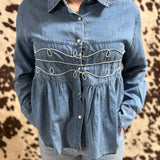 Full view of the shirt, shirt has a collar and 6 pearl snaps. Denim is light wash.