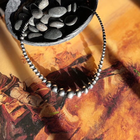 Full strand of graduated Navajo style pearls that range from 3mm to 14mm with the biggest pearls being in the center, necklace is draped over a woven basket.