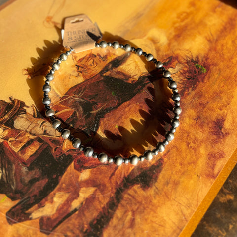 Full strand of Navajo st6yle pearls with alternating 6mm and 10mm size beads. Necklace is laying flat in a western designed table. 