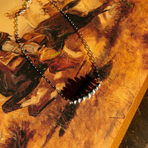 Navajo style pearl bar necklace with seven Navajo pearls slightly graduated and a sterling silver chain, necklace is laying flat on a western designed table.