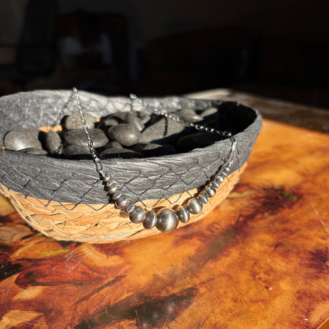 Navajo style pearl curved bar necklace with graduated sized pearls and detailed pearl accents and a sterling silver chain. Necklace is laying over woven basket.