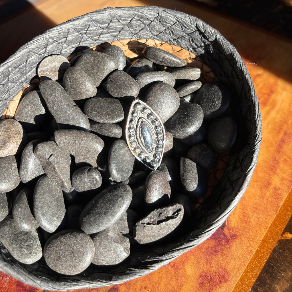 Silver marquise ring with silver studded accents, ring is sitting in a basket with black stones. 