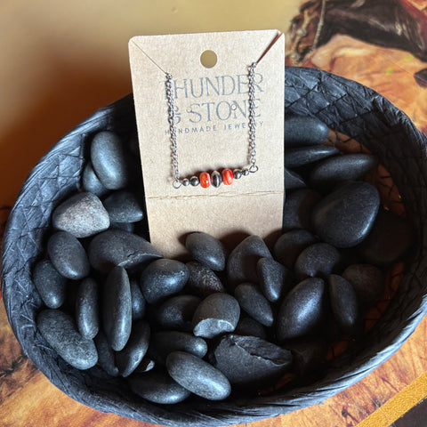 Sterling silver chain necklace with a small Navajo style pearl bar with two spiny stones, necklace is attached to a Thunder & Stone label and sitting in a basket with black stones.