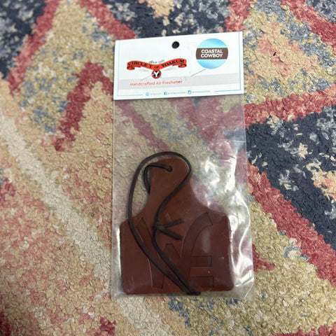 Leather air freshener in the shape of a cow ear tag. It has a large Western Edge logo on the front and a leather string at the top for hanging. 