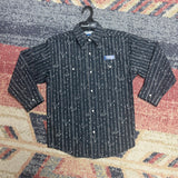 Long sleeve pearl snap laying flat on the ground, Shirt is black with white vertical barbed wire stripes with cowboy hats and steer skulls. 