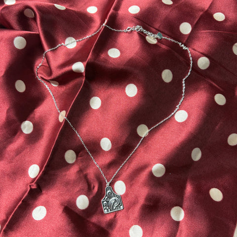 Small chain necklace with a silver tooled cattle ear tag pendant. 