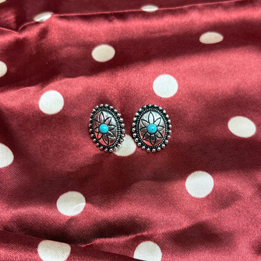 Set of silver oval earrings with a stamped flower design and a turquoise stone in the middle. 