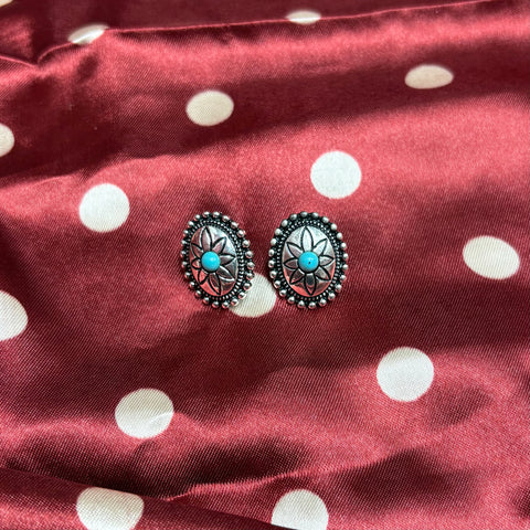Set of silver oval earrings with a stamped flower design and a turquoise stone in the middle. 