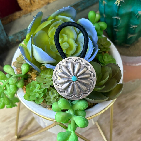 Black elastic hair tie with a circle Concho silver accent piece hat has stamped detailing and a turquoise stone in the middle.