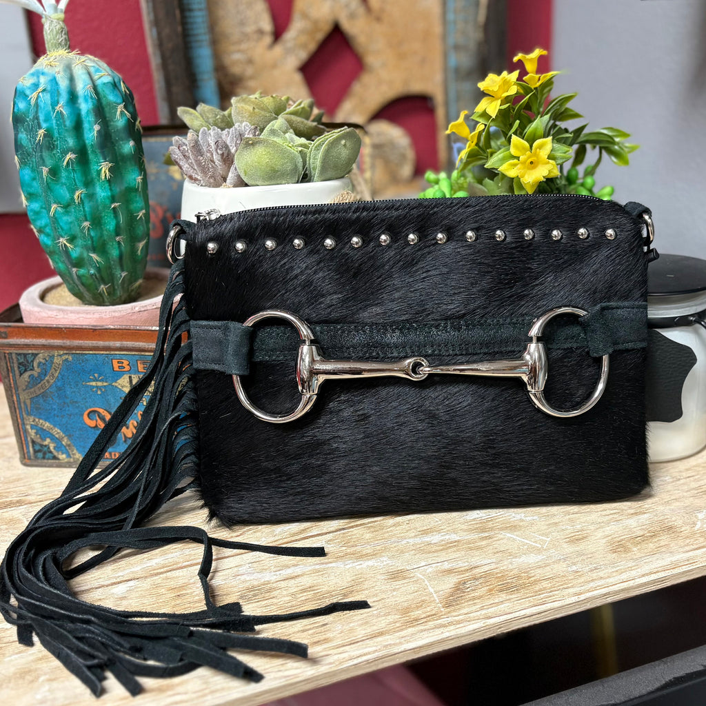 Black cowhide purse with a large silver horse bit on the front, silver studs on the top, and long black fringe on the side. 