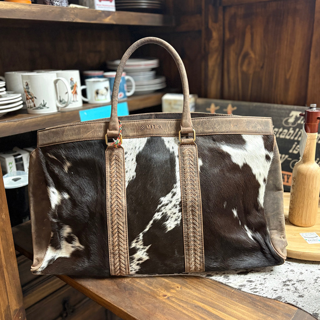 Large travel bag with black and white cowhide with brown leather handles. 