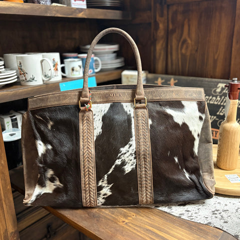Large travel bag with black and white cowhide with brown leather handles. 