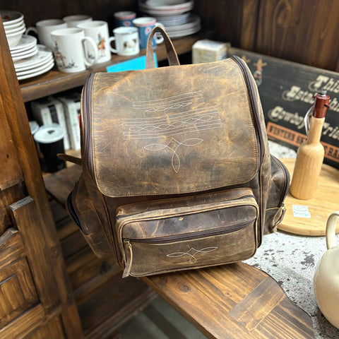 Rustic brown leather backpack with white boot stitching on the top and front pocket. 