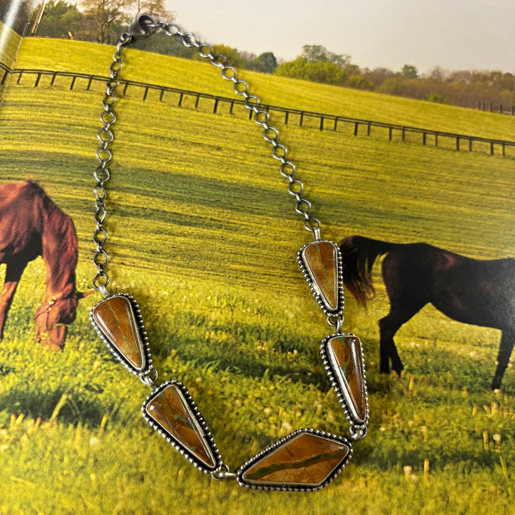 "Logie" Boulder Turquoise Oblong Choker laying on top of a scenic western picture 