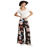 Woman wearing a white top and black patterned pants with cowboy-themed graphics