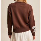 woman wearing a brown sweater with a big horseshoe on the front with bow patterns on sleeves back view