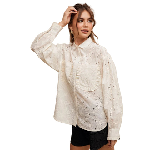 Woman wearing an off white lace button down blouse with ruffle chest pockets.