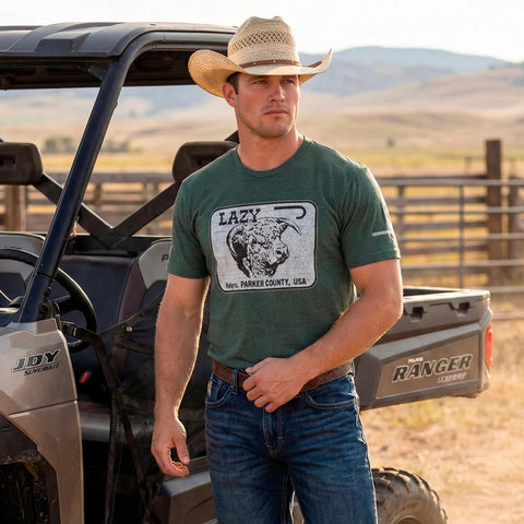 Model wearing the forest green Lazy J Ranch Parker County Hereford T‑shirt in a casual outdoor setting, showing the soft fabric and Western graphic style.