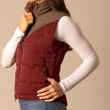 Side view of a  woman wearing a burnt red colored puffer vest with chocolate yoke.