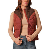 A woman wearing a burnt red colored puffer vest with chocolate yoke.