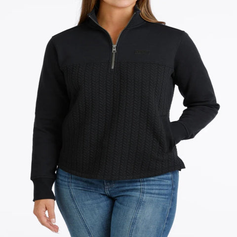 Woman wearing a black quarter-zip pullover with a textured cable-knit front, stand collar, side pockets, and subtle CINCH logo.