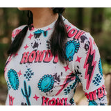 Close up view of cream-colored mesh long sleeve with pink and teal western designs. Includes the word "Howdy" in pink lettering. 