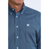 Close up of man wearing blue geometric long sleeve shirt with white buttons and white cinch logo.