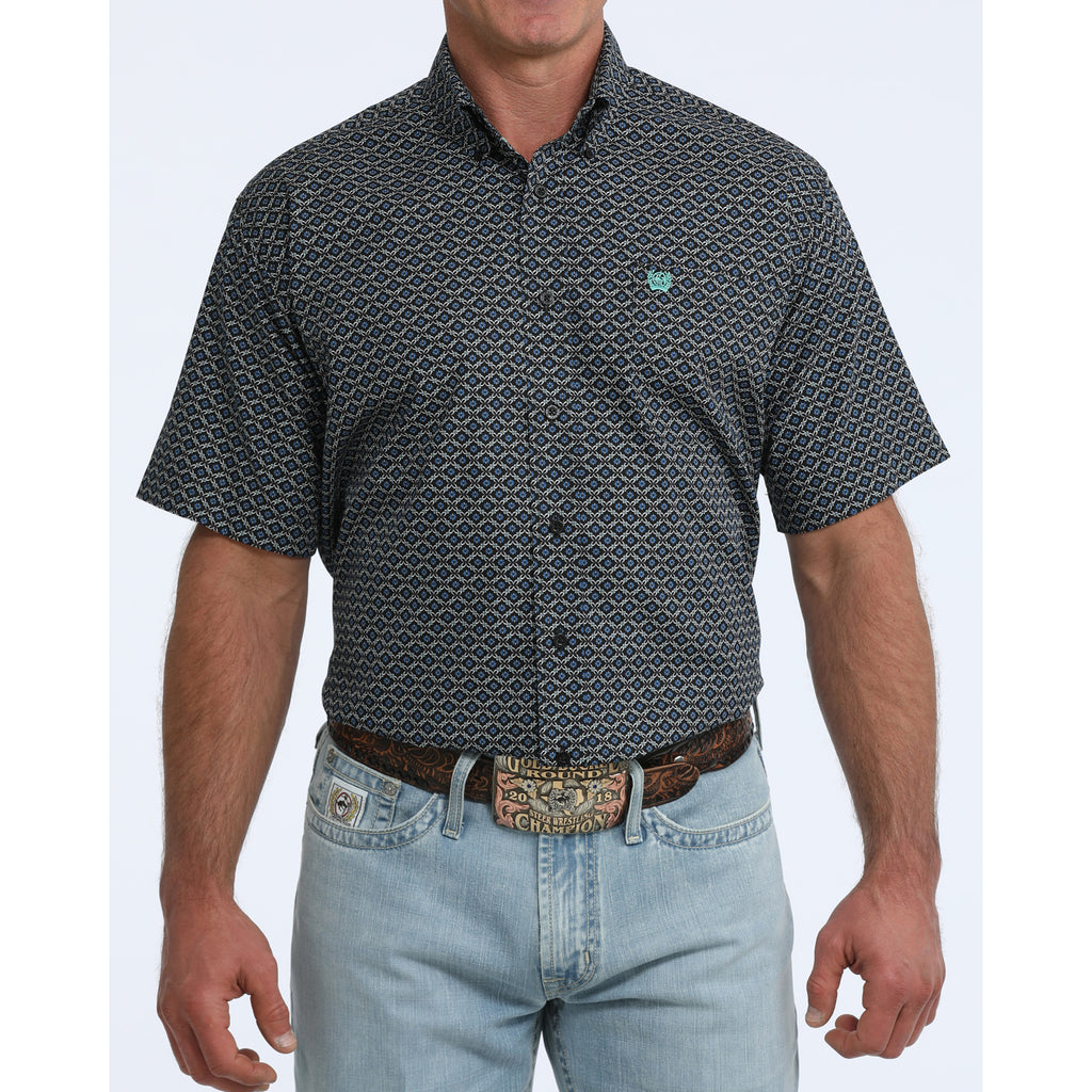 Front view of man wearing a black short sleeve shirt with turquoise geometric print standing in front of white background.