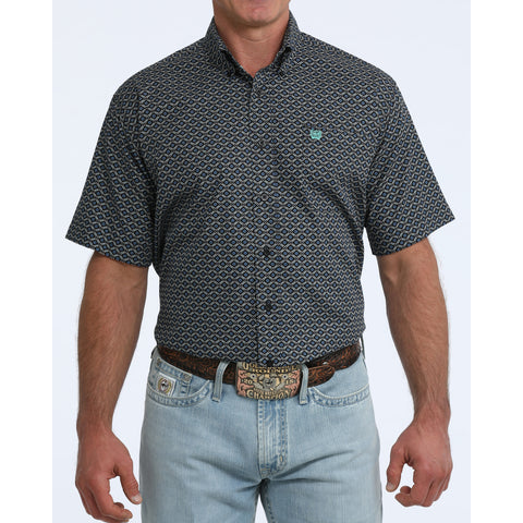 Front view of man wearing a black short sleeve shirt with turquoise geometric print standing in front of white background.