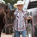  Model wearing kids’ western striped pearl snap shirt in white, purple, and grey, leading a horse.