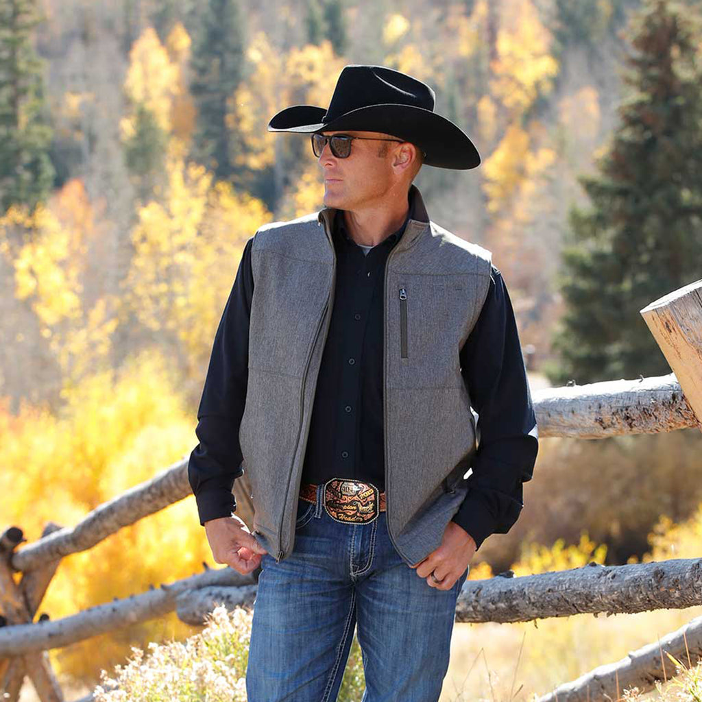 Man wearing a black cowboy hat, black shirt and a grey vest with olive accents.