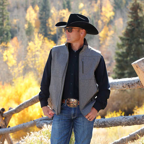 Man wearing a black cowboy hat, black shirt and a grey vest with olive accents.