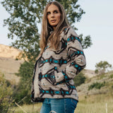 Woman wearing light brown and turquoise Aztec jacket in rustic outdoor setting