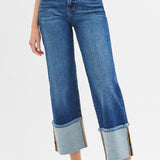 Model wearing jeans with one leg forward, medium wash color and high sewn cuff at the bottom.
