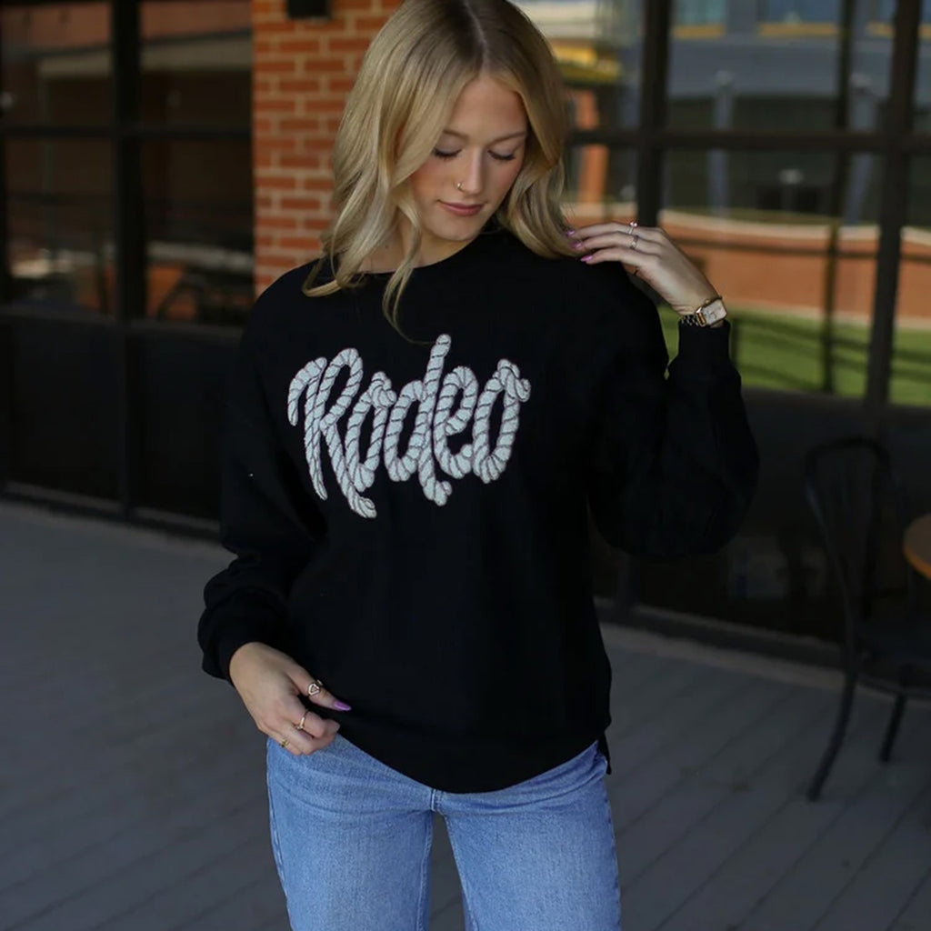 Black long sleeve sweater with a "Rodeo" motif written in rope like font. 